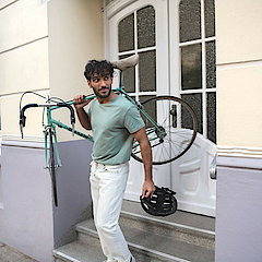 Ein Mann trägt rechts sein Fahrrad und steht auf einer Treppe. Er wendet den Blick nach links.