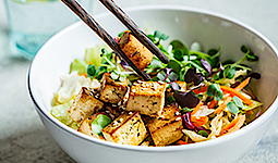 Lecker aussehender asiatischer Salat mit gebratenem Tofu. Ein Tofuwürfel wird von zwei Essstäbchen gehalten.
