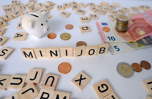 Zu sehen sind Buchstaben aufgestellt als Minijob, ein Sparschwein und Euroscheine, Münzen