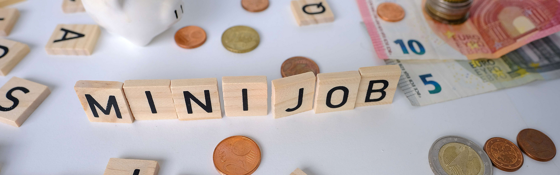 Zu sehen sind Buchstaben aufgestellt als Minijob, ein Sparschwein und Euroscheine, Münzen