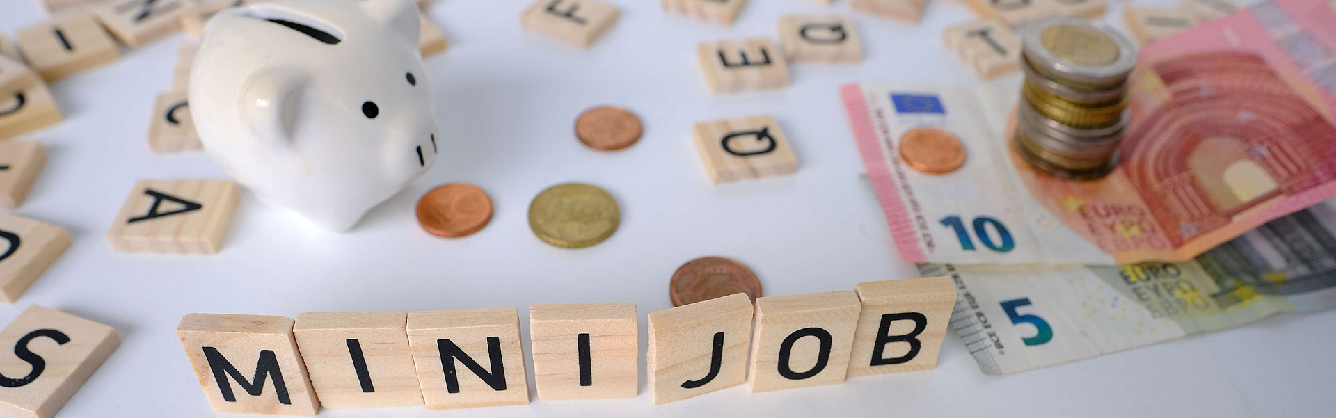 Zu sehen sind Buchstaben aufgestellt als Minijob, ein Sparschwein und Euroscheine, Münzen