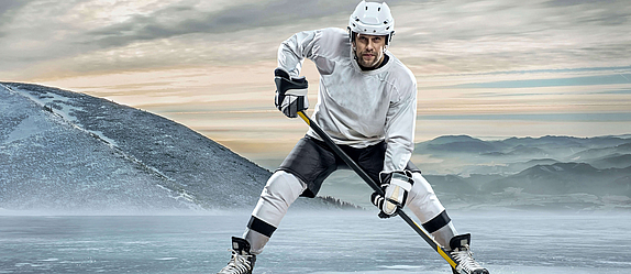 Ein Eishockeyspieler steht auf dem Eis. Er ist zum Angriff bereit. Der Schläger ist gesenkt. Vor ihm liegt der Puk.