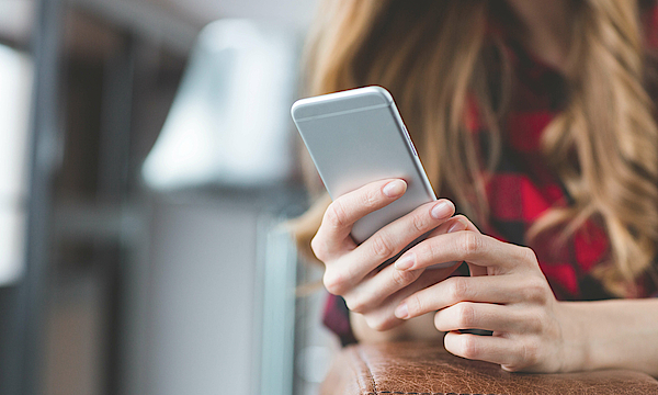 Blonde Frau mit einem Smartphone in der Hand. Man kann nur die Hände und das Smartphone sehen.