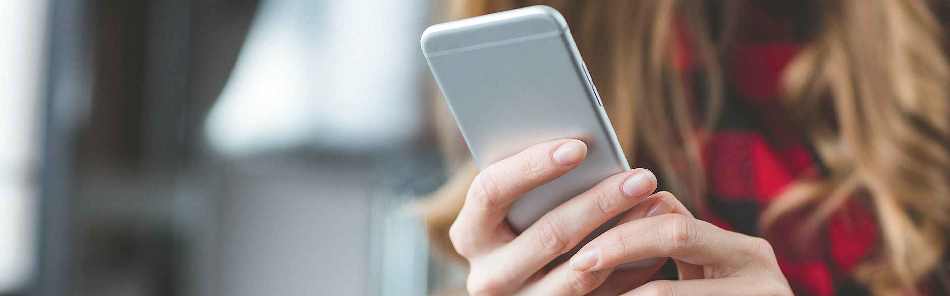 Blonde Frau mit einem Smartphone in der Hand. Man kann nur die Hände und das Smartphone sehen.