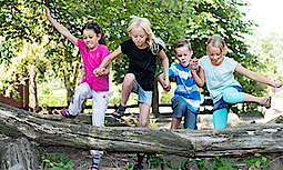 Vier Kinder springen gemeinsam über einen Holzstamm