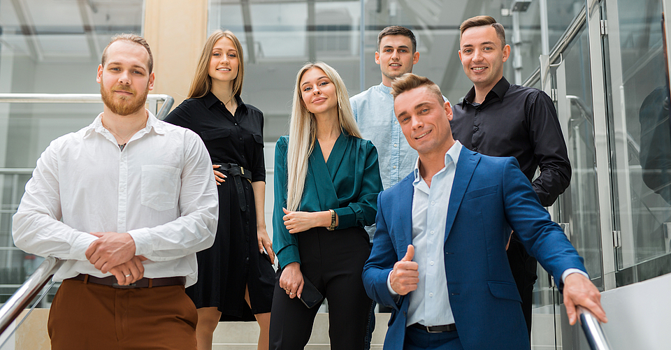 Eine Gruppe junger Menschen steht auf einer Treppe. Sie haben ihren ersten Arbeitstag.