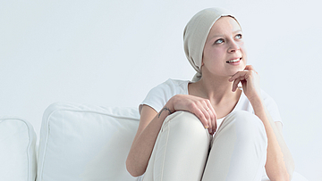 Eine kranke Frau schaut nachdenklich aus dem Fenster.