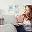 Frau sitzt auf dem Sofa und arbeitet mit dem Laptop. Der Laptop ist auf dem Sofa abgelegt.