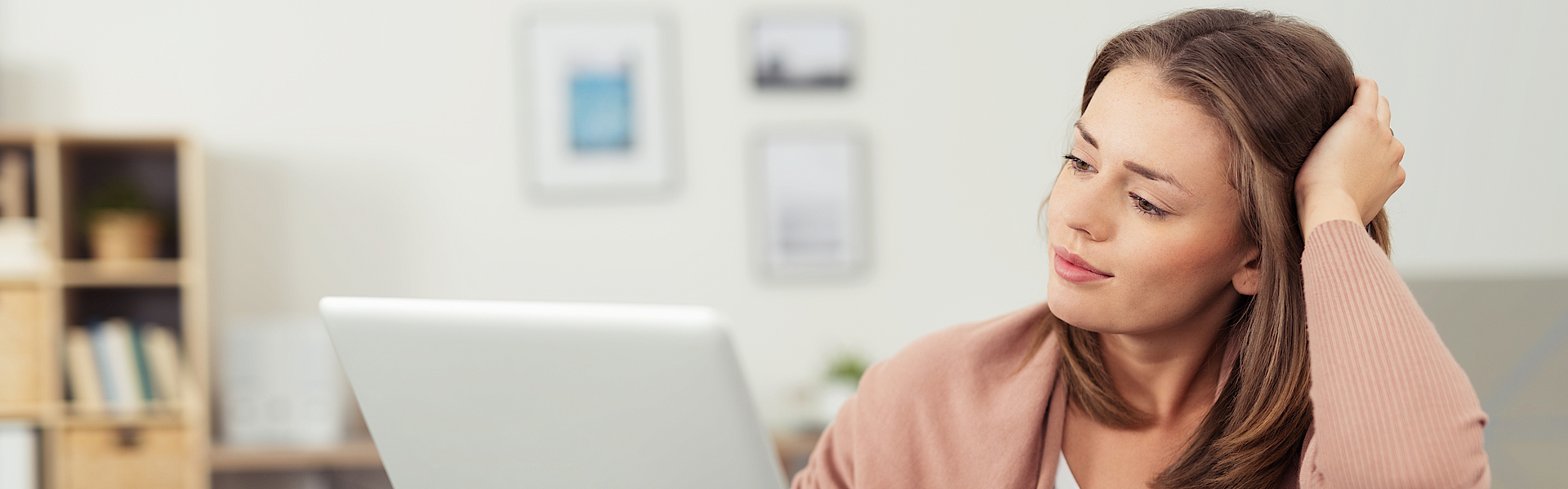 Frau sitzt auf dem Sofa und arbeitet mit dem Laptop. Der Laptop ist auf dem Sofa abgelegt.