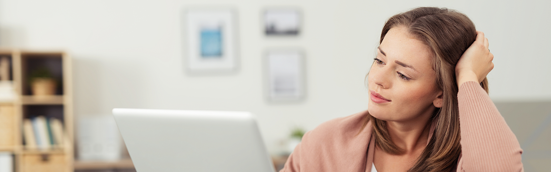 Frau sitzt auf dem Sofa und arbeitet mit dem Laptop. Der Laptop ist auf dem Sofa abgelegt.