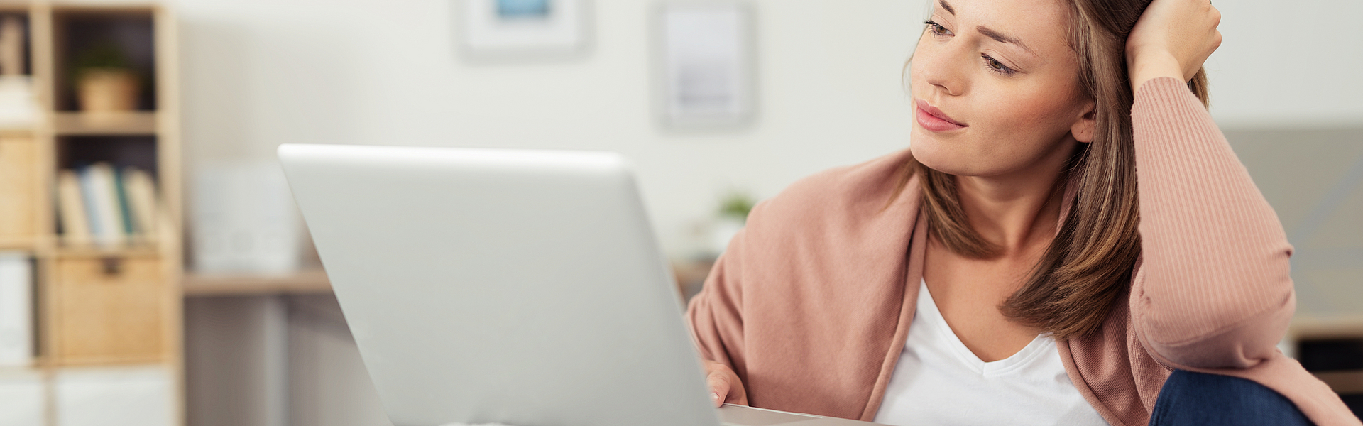 Frau sitzt auf dem Sofa und arbeitet mit dem Laptop. Der Laptop ist auf dem Sofa abgelegt.