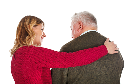 Frau und älterer Mann stehen mit dem Rücken zum Bild. Die Frau umarmt den Mann.