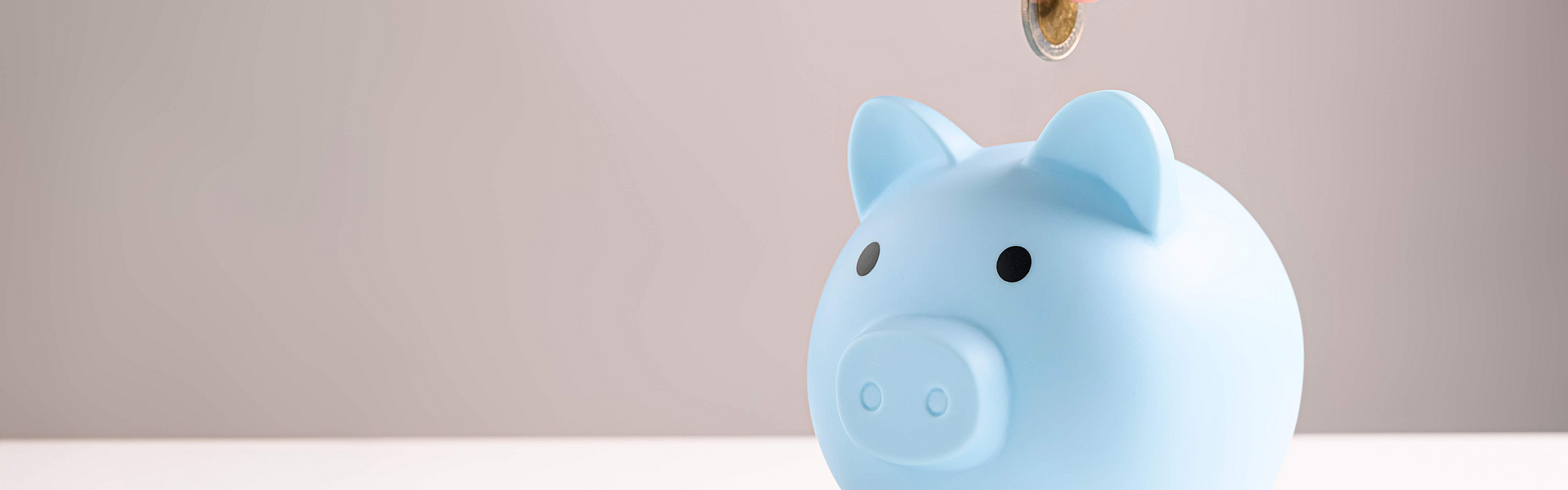 Hand steckt Kleingeld in blaues Sparschwein