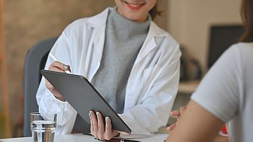 Ein Arztgespräch mit Patient. Der Arzt hat ein Tablet in der Hand und zeigt etwas dem Patienten.