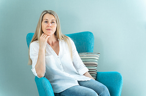 Frau im mittleren Alter sitzt in einem blauen Sessel