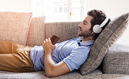 Mann zu Hause auf dem Sofa und hört Musik mit Smartphone