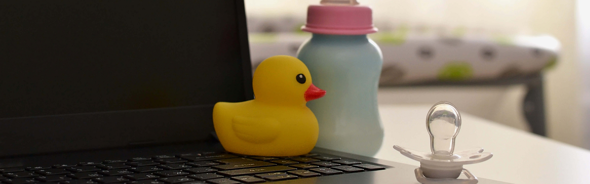 Schnuller am Laptop und Babyflasche. Arbeiten in einem Dekret. Konzept des Mutterschaftsurlaubs.