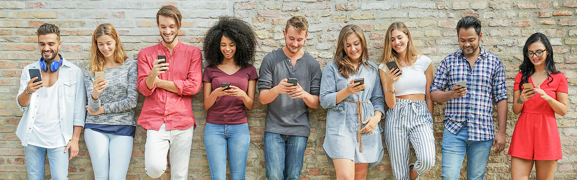 Eine Gruppe junger Menschen steht vor einer Mauer. Jeder hat ein Smartphone in der Hand und blickt darauf.