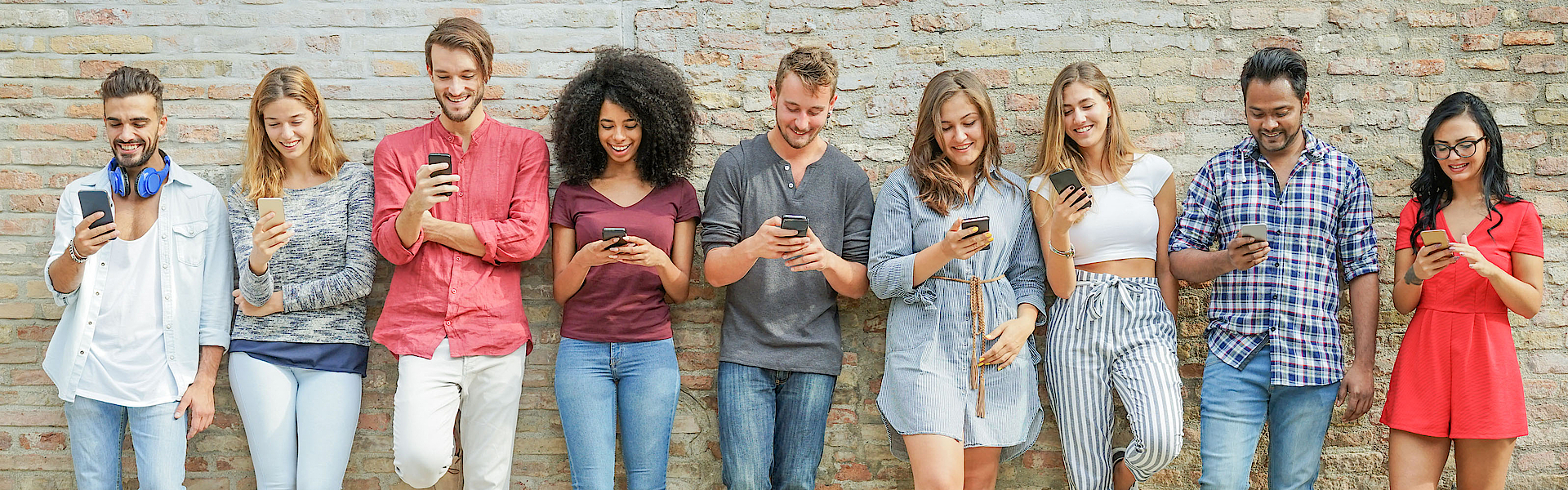 Eine Gruppe junger Menschen steht vor einer Mauer. Jeder hat ein Smartphone in der Hand und blickt darauf.