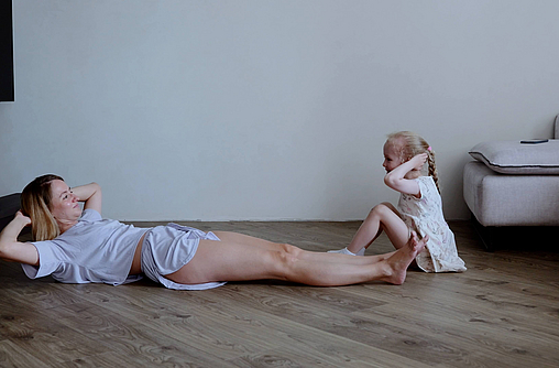 Mutter und kleine Tochter machen Gymnastik auf dem Fußboden 