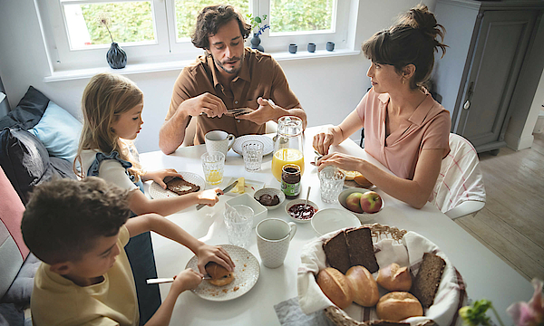 Eine Familie sitzt gemeinsam am Frühstückstisch und genießen das gemeinsame Essen.