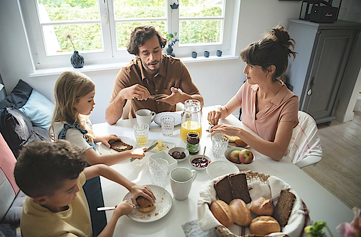 Eine Familie sitzt gemeinsam am Frühstückstisch und genießen das gemeinsame Essen.