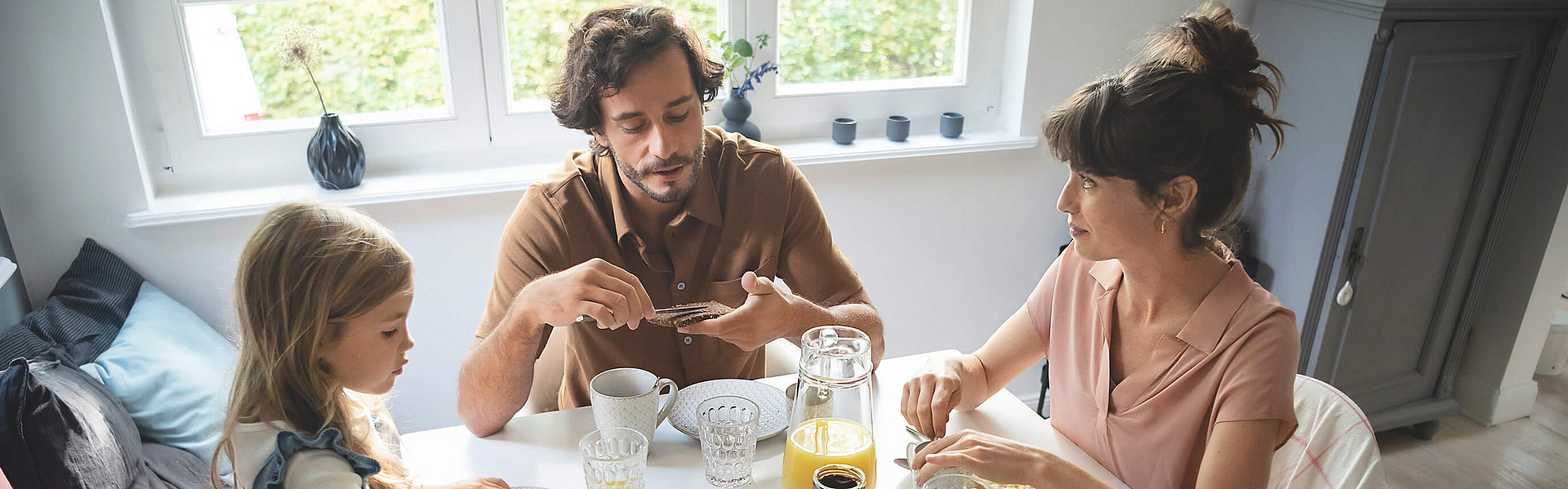 Eine Familie sitzt gemeinsam am Frühstückstisch und genießen das gemeinsame Essen.