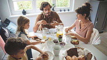 Eine Familie sitzt gemeinsam am Frühstückstisch und genießen das gemeinsame Essen.