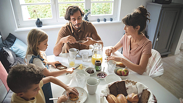 Eine Familie sitzt gemeinsam am Frühstückstisch und genießen das gemeinsame Essen.