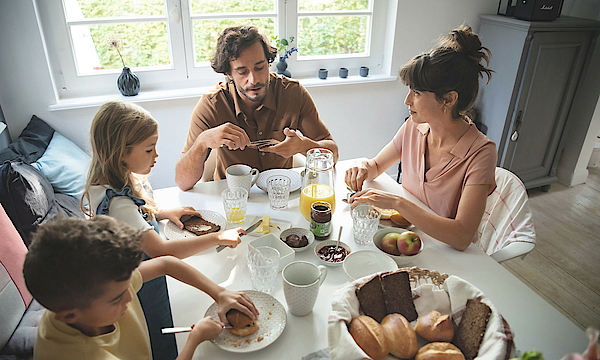 Eine Familie sitzt gemeinsam am Frühstückstisch und genießen das gemeinsame Essen.