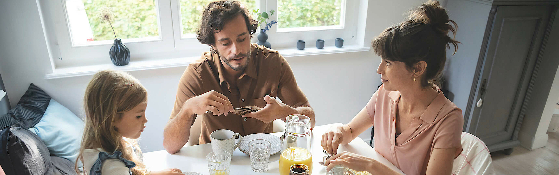 Eine Familie sitzt gemeinsam am Frühstückstisch und genießen das gemeinsame Essen.