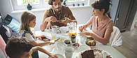 Eine Familie sitzt gemeinsam am Frühstückstisch und genießen das gemeinsame Essen.