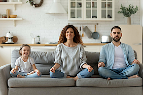 Junge Familie mit kleiner Tochter versuchen eine Yoga Entspannungsübung auf einem Sofa.