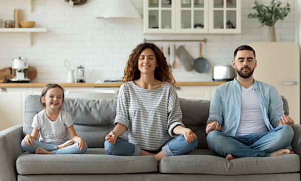 Junge Familie mit kleiner Tochter versuchen eine Yoga Entspannungsübung auf einem Sofa.