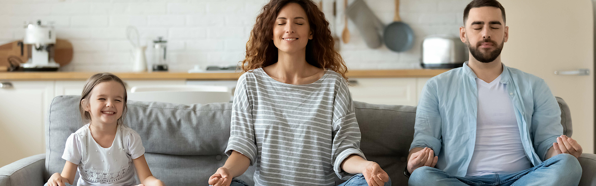 Junge Familie mit kleiner Tochter versuchen eine Yoga Entspannungsübung auf einem Sofa.