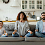 Junge Familie mit kleiner Tochter versuchen eine Yoga Entspannungsübung auf einem Sofa.