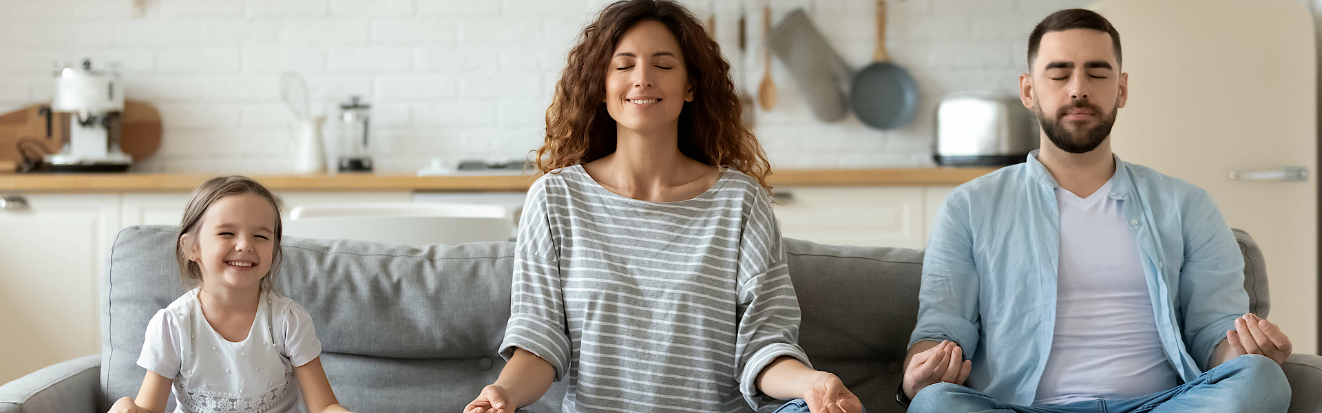 Junge Familie mit kleiner Tochter versuchen eine Yoga Entspannungsübung auf einem Sofa.