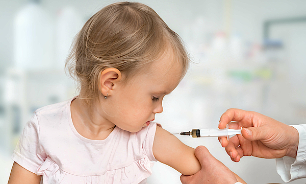 Kleines Mädchen beobachtet wie sie eine Impfung bekomnmt. 