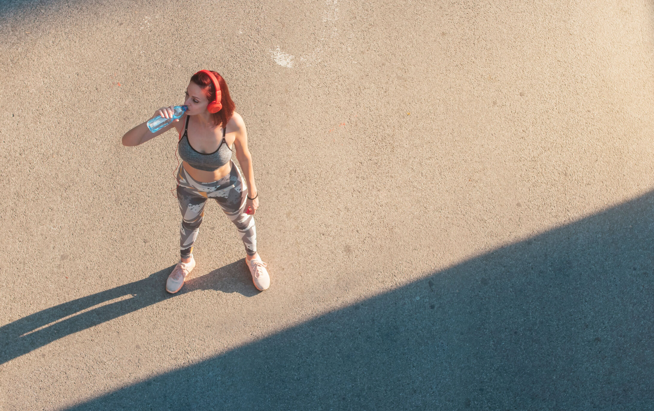 Frau in Sportkleidung steht in der Sonne und trinkt nach dem Sport