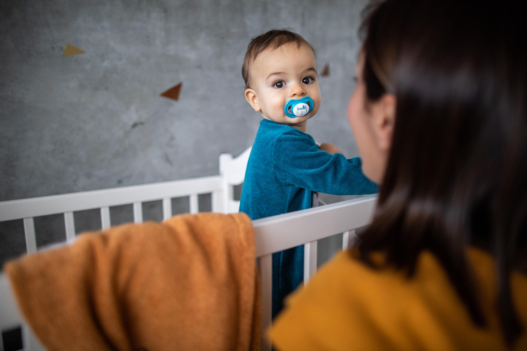 Kleinkind steht im Kinderbett, die Mama lächelt es an